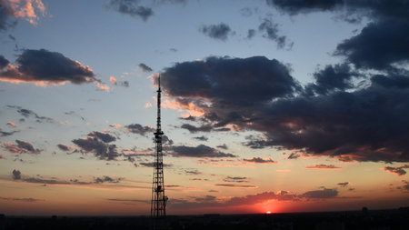 Cloudscape with industrial communication tower and dark purple clouds while golden sunbeams shining...