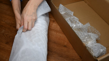 Hands hold packing material and wrap glassware into soft packing due to prepare for moving day....