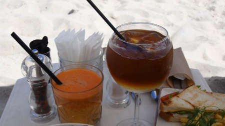 Closeup table setting with fresh vegetable salad, club sandwiches with French fries and summer cocktails. Waiter hands put cutlery on table. Catering outdoor at sunny day on beachの写真素材