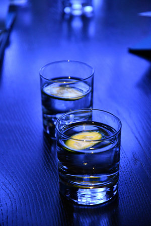 Two glasses of still water with cucumber pieces to refresh. Vibrant blue neon lighting to summer...