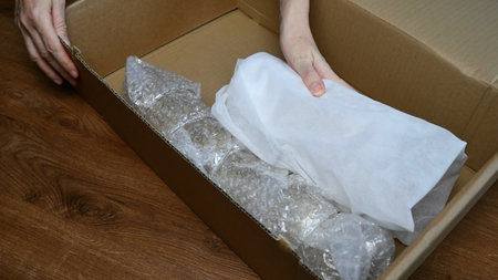 Female hands pack up fragile tableware into wrapping bubble plastic and packing wrappings and put...