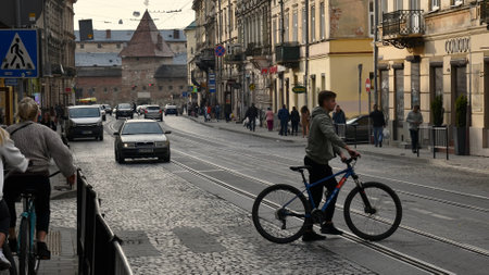 European town street. City traffic and man with bicycle walking by pedestrian crosswalk over cobblestone road of ancient architecture cityscape. Lviv, Ukraine 10 09 2020のeditorial素材