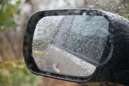 Blurry glass with rain drops rolling on window, and car side view mirror with defocused reflectionsの写真素材
