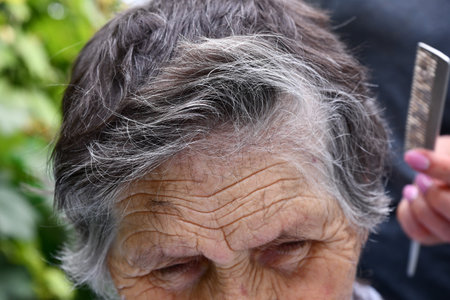 Deep wrinkles on aged skin of forehead 80s woman while cutting her gray hair. Cut off ends of hair cover elderly skin of granny faceの写真素材