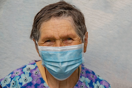 Senior woman wear disposable medical mask on her aged face. Elderly woman in single-use mask. Aged wrinkled face of 80 year old woman with short gray haircutの写真素材