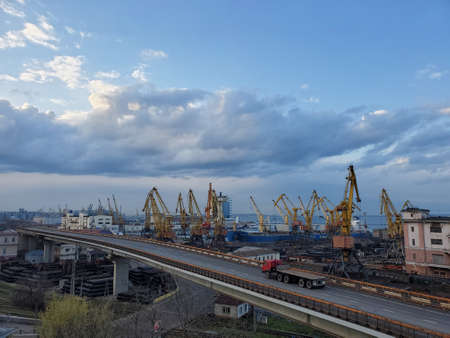 Red trailer drive by overpass road. Maritime port landscape with yellow cargo cranes at waterfront and cloudscape aboveの写真素材