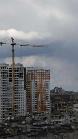 Construction site of unfinished multistory building with crane jib at overcast sky background. Under construction cityscape with rooftops and cloudscape. Vertical shotの写真素材