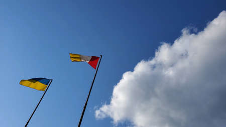 Ukrainian flag and Odessa flag wave in wind on sky background at sunny day. Yellow blue striped flag of Ukraine country of Eastern Europe. Yellow, white and red flag of Odessa cityの写真素材