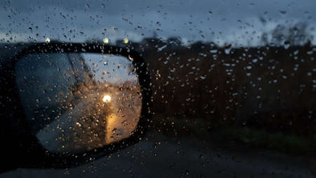 Wet glass texture with raindrops on window. Car side view mirror with defocused reflections and blurred background of autumn night with defocused car lightsの写真素材