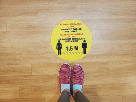 POV feet wearing pink sport shoes stand by yellow sticker warning of keeping social distance in Turkish, English, German, Russian. Social distancing caution sign on floor. Text - keep social distanceの写真素材