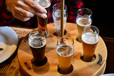 Female hand takes glass of craft beer in pub to make toast cheers. Drinking various types of craft beer including stout, lager, ale, pilsner and weiss. People enjoying beer. Kyiv, Ukraine, 07 21 2021のeditorial素材