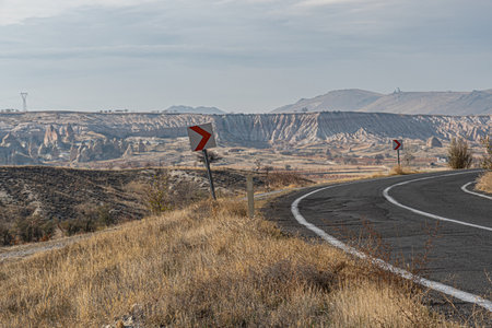 Curved turn of open road with road signs and nobody at mountain landscape of Cappadocia Turkey. Travel concept. Autumn dried grass at roadside with arrow road signs by road sideの写真素材