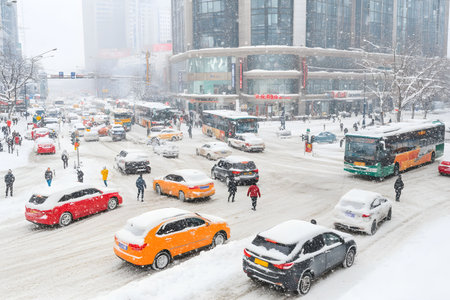 Heavy snowfall blankets the city streets, creating a chaotic scene as vehicles navigate through deep snow. Pedestrians struggle against blizzard conditions, while buses and cars are stuck.の素材