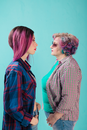 Young girl and happy senior woman in colorful casual clothes. Two generations of hipsters. Stylish senior woman on blue background. Common colorful hair and informal lifestyle of two generationsの写真素材