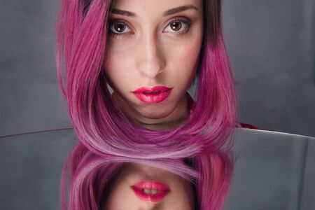 Sensual young woman model with pink hair and make-up on the face. Red lips over the mirrorの写真素材