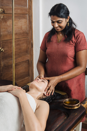 Ayurvedic face massage with oil on the wooden table in traditional style made by asian women.の写真素材