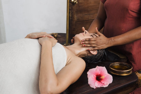 Ayurvedic face massage with oil on the wooden table in traditional style made by asian women.の写真素材