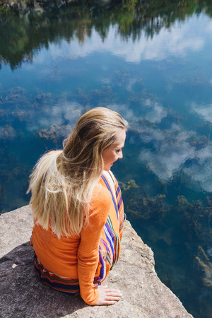 Beautiful blonde woman enjoying blue lake water on the high cliff in summer. Concept of freedom outdoorsの写真素材