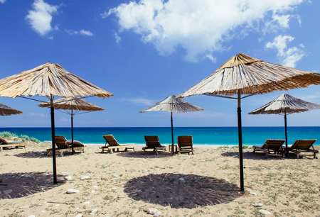 Early season on sandy beach near deep blue sea. Natural cane umbrellas and empty deck chairs with beautiful landscape. Tranquil, serene recreation place in Turkey.の写真素材