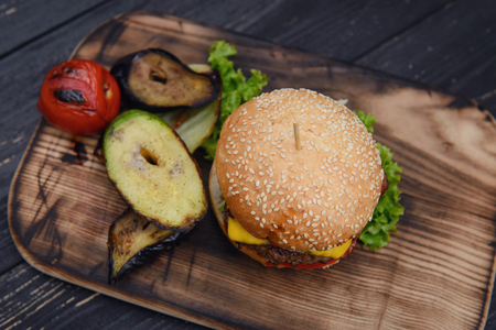 Cheeseburger on the wooden table outdoors. served with grilled vegetables. Home made fast food from fresh, tasty ingredients. Hamburger with crispy beckon and tomato insideの写真素材