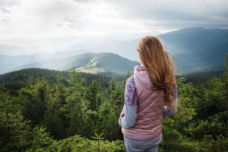 Woman looking on cloudy, mountain landscape and feeling freedom during tripの写真素材