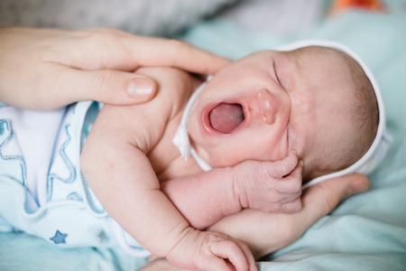 Newborn baby sleeping and yawning wide. Parent's hand touching childの写真素材