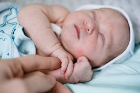 Newborn baby sleeping at home. Parent's hand touching child hand and small fingersの写真素材