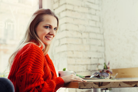 Young romantic woman sitting at a cafe having morning latte over brick wallの写真素材