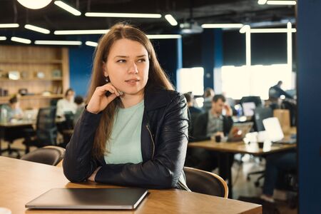 Freelancer woman working at co-working or creative space, sitting near laptop over group of peopleの写真素材