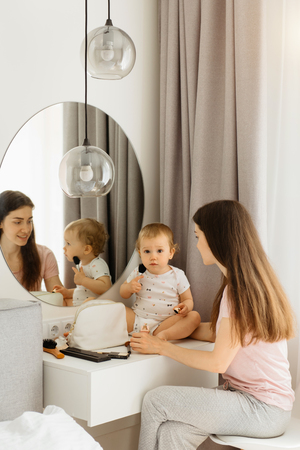 Funny family at home. Daughter uses brash on mother's face at home near the mirrorの写真素材