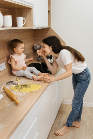 Family having fun on the kitchen. Mother and baby girl making homemade cookies. Kid is playing with dough and parentsの写真素材