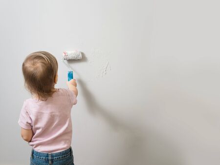 Little child painting the wall with roller and light gray paint, empty background. Interior decoration, redesign, Copy spaceの写真素材