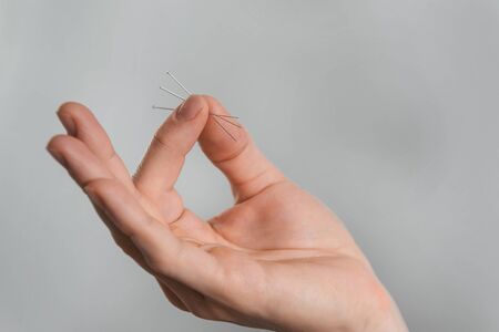 Acupuncture needles in hands over grey background. Alternative chinese medicine, relieve painの写真素材