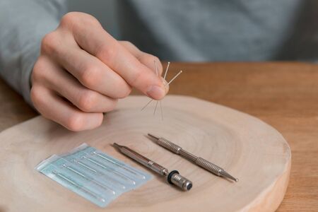 Acupuncture treatment on mans hands. Rehabilitation using alternative medicine. Acupressure instruments on wooden background.の写真素材