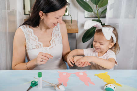 Child with mother making Easter gift or decoration with a bunny from paper at home. Handmade. Project of childrens creativity, handicrafts, crafts for kid, toddler.の写真素材