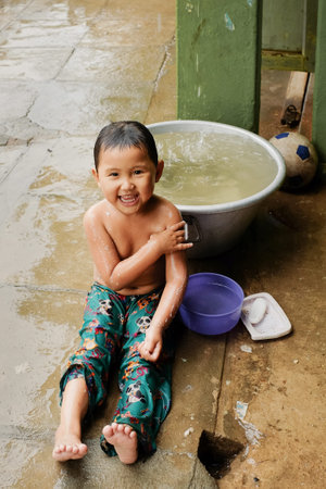 Bagan, Myanmar: May, 25, 2016. Child washing under the rain on the street of Bagan. Happy pour Asian...