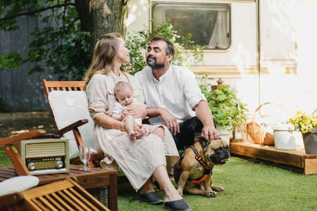 Family with baby and dog spending happy time together near trailer outside on deck chair, traveling lifestyle with camperの写真素材