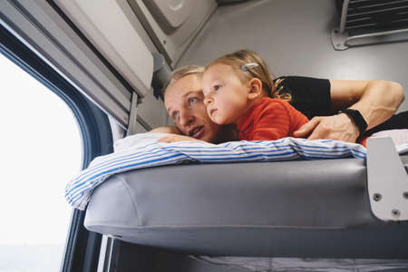 Father with child travalling in the train, having fun enjoying scene through window while riding on railroad togather in sleeping carの写真素材