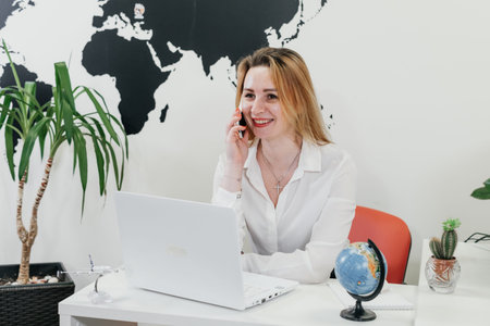 Happy businesswoman travel agent using laptop and smartphone for communication and work on-line in...