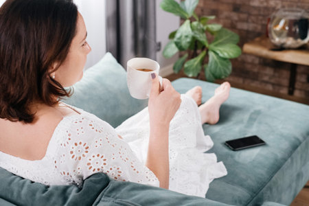 Woman drinking mug of coffee in cozy home atmosphere in the morning. Real middle age plus size...