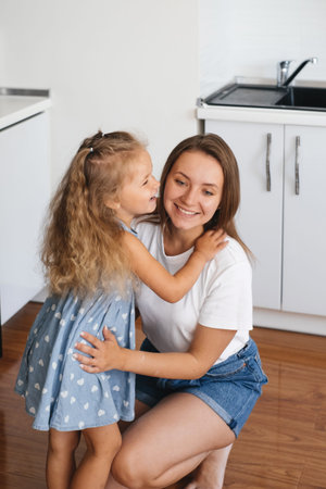 Child whispering something on Mothers ear at home on the kitchen. Kid telling a secret. Toddler girl...