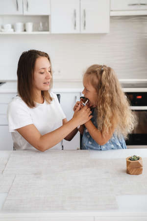 Child is having sweet snack on the kitchen. Happy toddler kid having tasty candy with mother at home. Caucasian blonde familyの写真素材