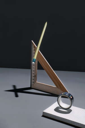 Concept of work or education. Trendy, creative dark composition in office with shadows. Balancing objects on the table: pencil, ruler, tape, notepad on the desk, minimalistic style.の写真素材