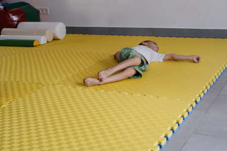 Child on the mat in child rehabilitation center. Boy with cerebral palsy laying down. Rehabilitation and inclusion kindergarten, day care. Disabled boyの写真素材