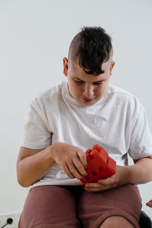 Disabled teenage child build from blocks Boy with cerebral palsy doing activities for Children with Special Needs over white background. creativity, fine motor skills, rehabilitation, learning at homeの写真素材