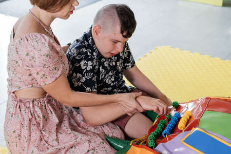 Children with disability getting sensory activity with toys, balls, small objects, cerebral palsy boy playing calming game, training fine motor skills. Rehabilitation center with therapist, motherの写真素材