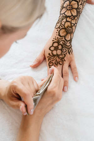 Artist applying henna tattoo on women hands. Mehndi is traditional Indian decorative art, Hand with floral mehendi. Beauty drawing for weddings and festivals using paste from powdered dry plantの写真素材