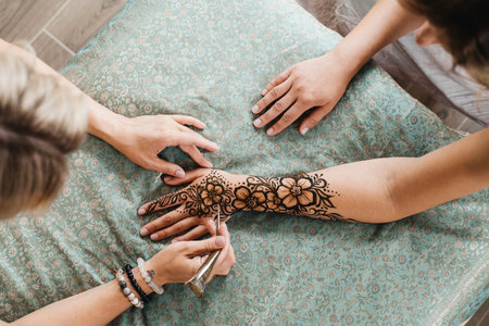 Artist applying henna tattoo on women hands. Mehndi is traditional Indian decorative art, Hand with floral mehendi. Beauty drawing for weddings and festivals using paste from powdered dry plantの写真素材