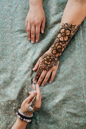Artist applying henna tattoo on women hands. Mehndi is traditional Indian decorative art, Hand with floral mehendi. Beauty drawing for weddings and festivals using paste from powdered dry plantの写真素材