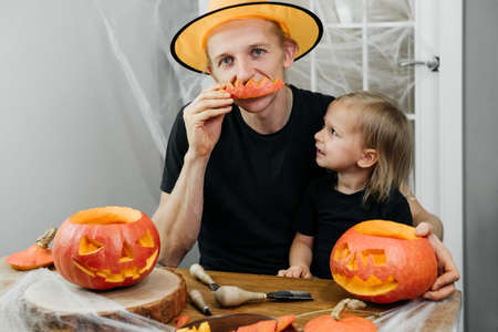 Parent with chld are carving jack o lantern from pumpkin for Halloween at home. Father in hat preparing for the selebration with daughter.の写真素材